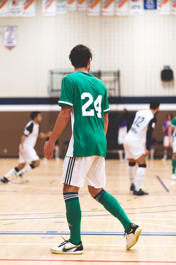 Dynamic indoor soccer match featuring players in green and white uniforms competing vigorously.