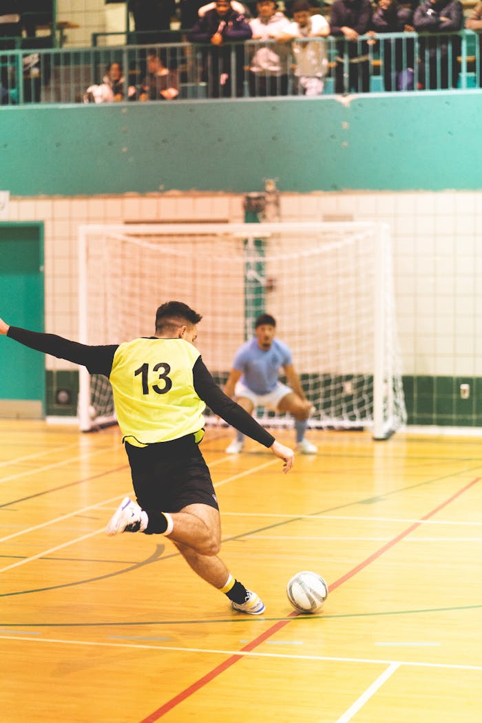 Player kicks the ball towards the goal in a competitive indoor futsal match.